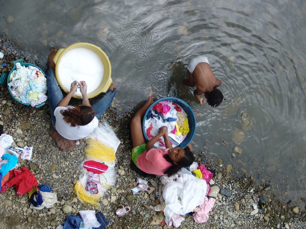 women washing clothes river poverty